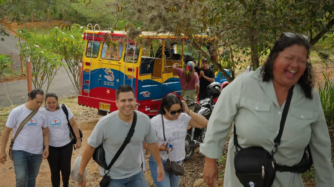 Un grupo de visitantes baja sonriendo de una chiva a la entrada de un sendero