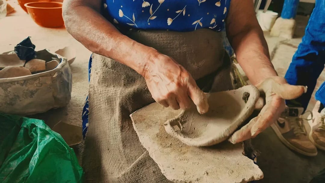 Las manos de una alfarera dando forma a una sartén de barro sobre un costal