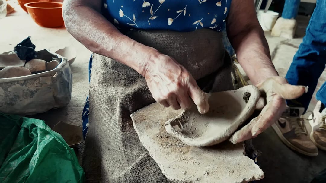Las manos de una alfarera dando forma a una sartén de barro sobre un costal